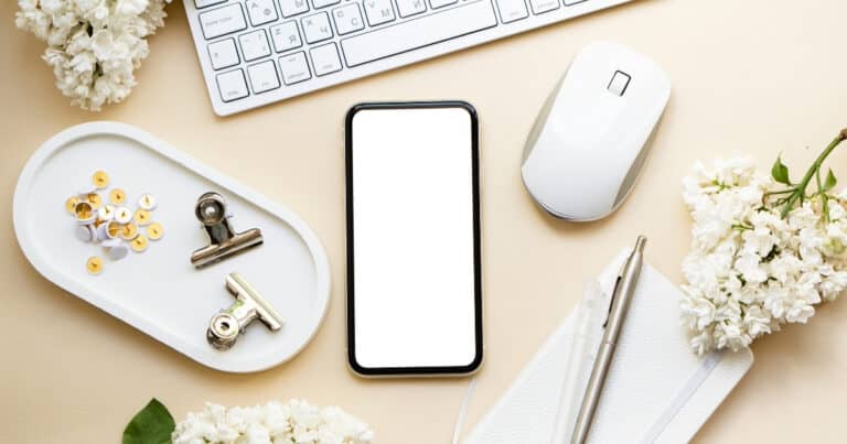 Desk with keyboard, mouse, cell phone, notebook, pen, and flowers