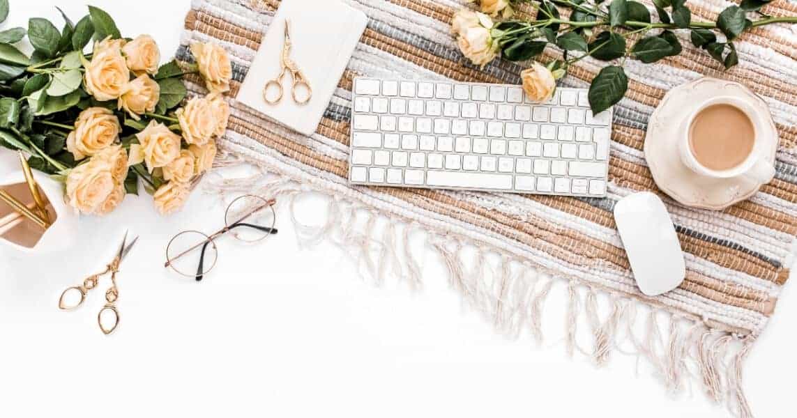 Desk with placemat, keyboard, glasses, coffee, paper, scissors, and flowers,