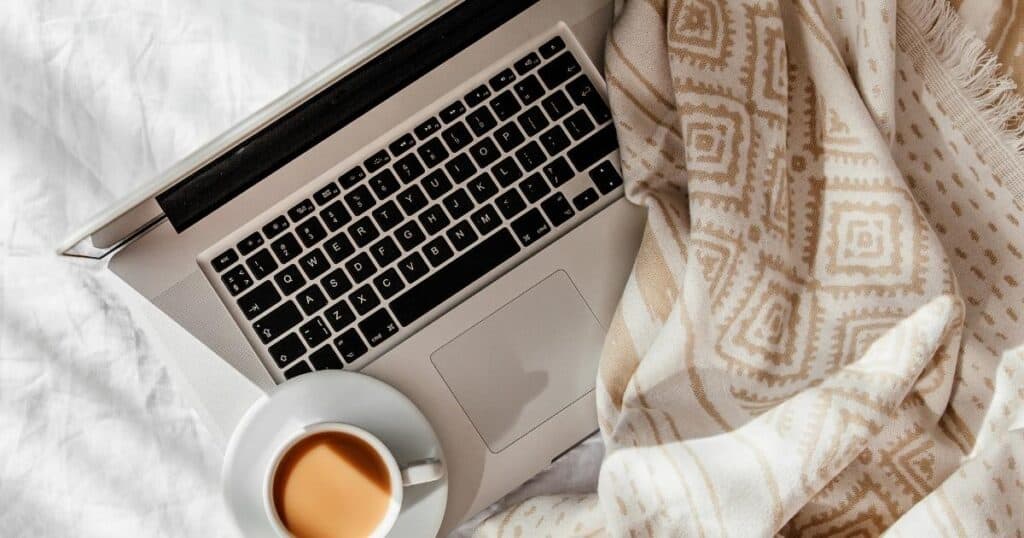 Laptop, coffee, and a throw sitting on a bed