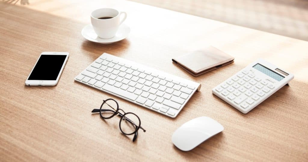 Desk with keyboard, mouse, cell phone, glasses, and coffee