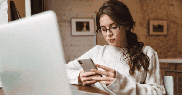 Woman sitting at a computer holding a cell phone