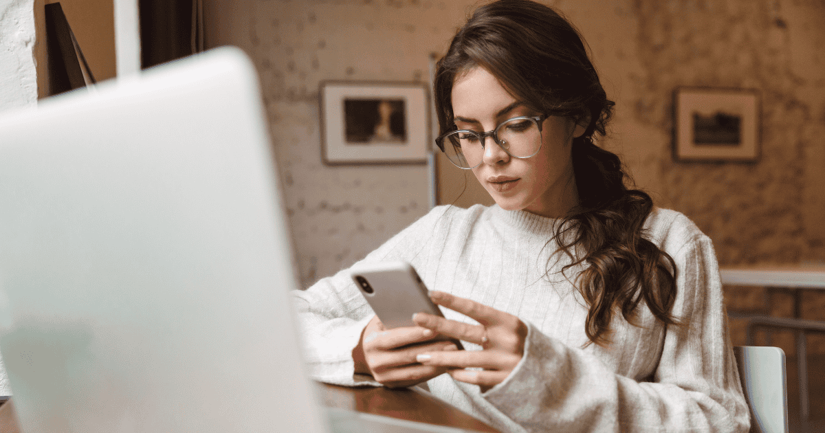 Woman sitting at a computer holding a cell phone